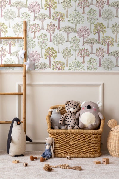 Kinderzimmer mit Mustertapete mit Bäumen, einer Bambusleiter und einem Korbsessel mit Kuscheltieren. Helle und ordentliche Gestaltung.