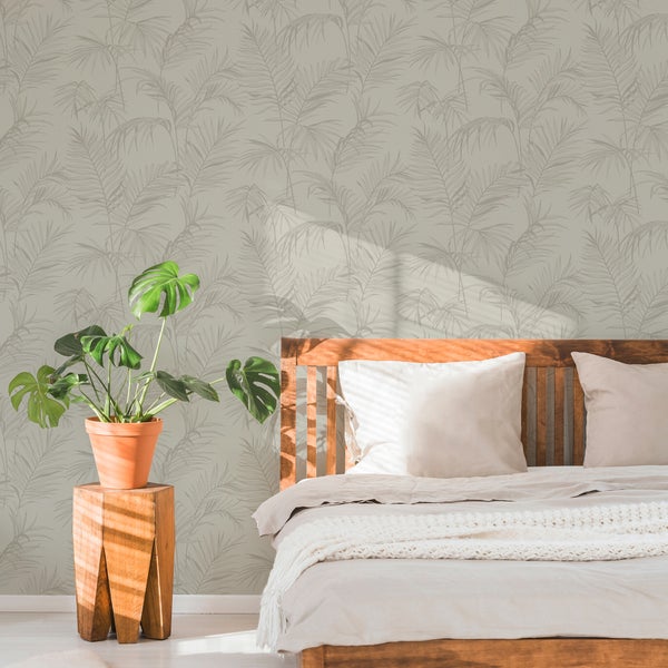 Vliestapete mit Palmenblattmuster in einem hellen Schlafzimmer mit Holzbett und einer Monstera Pflanze auf einem Holzhocker.