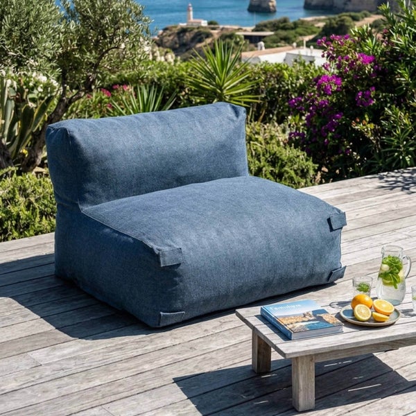 Moderner blauer Outdoor-Loungesessel auf einer Holzterrasse in einem hellen Garten mit Meerblick und Beistelltisch.