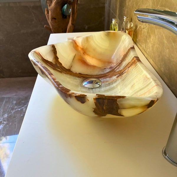 Aufsatzwaschbecken aus Naturstein Onyx in organischer Form auf einer Waschtischplatte im Badezimmer.