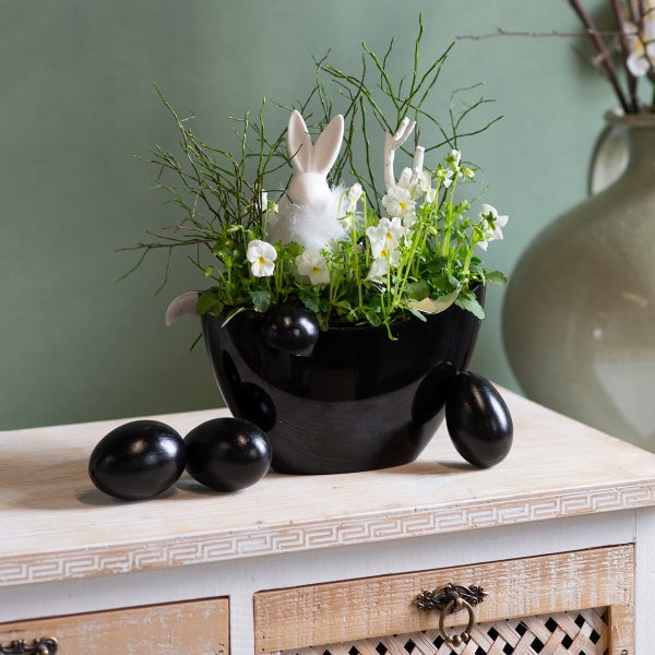 Osterdekoration mit Pflanzschale, weißem Hasen, Blumen und Eiern auf einer Kommode.