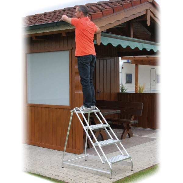Ein Mann steht auf einer stabilen Aluminium Stufenstehleiter vor einem Gartenhaus aus Holz, um die Dachrinne zu reinigen.