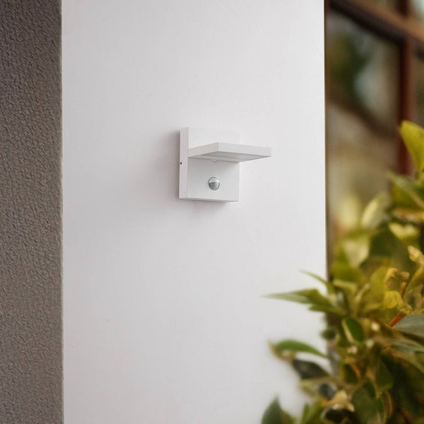 Moderne weiße Außenwandleuchte in quadratischem Design mit integriertem Bewegungsmelder an einer Hauswand montiert.
