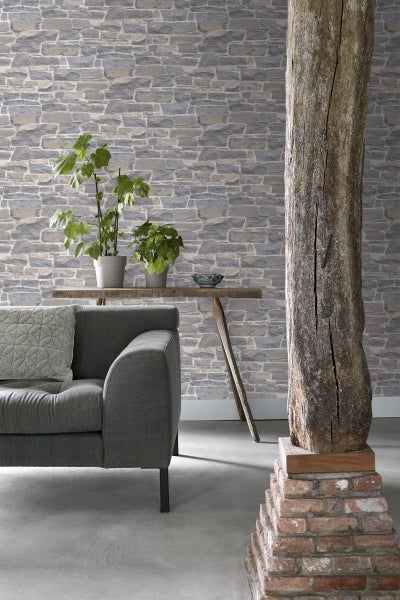 Wohnzimmer mit grauer Couch, Holztisch, Pflanzen und Tapete in Steinoptik