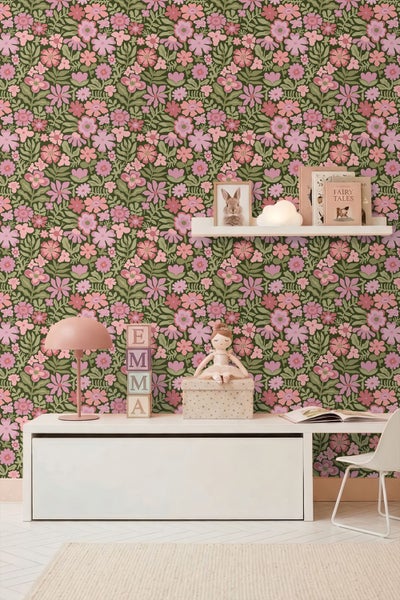 Kinderzimmer mit Blumentapete, die rosa Blüten auf grünem Grund zeigt. Auf einem weißen Schreibtisch stehen eine rosa Lampe und Spielzeug.