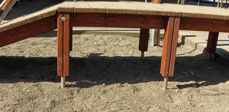 Holzpodest eines Spielgeräts mit Pfostenankern im Sand.
