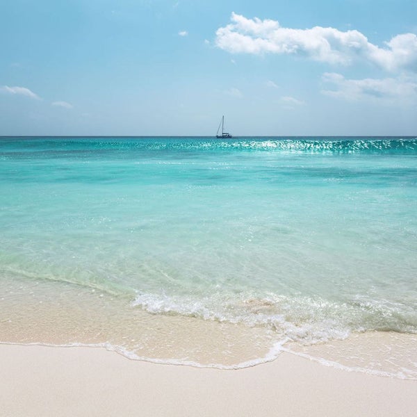 Ein Segelboot auf einem hellen Meer, gesehen von einem Strand aus.