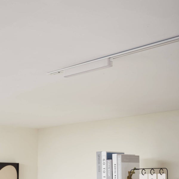 Modernes Schienensystem mit weißer, linearer LED-Leuchte an der Decke über einem Bücherregal.