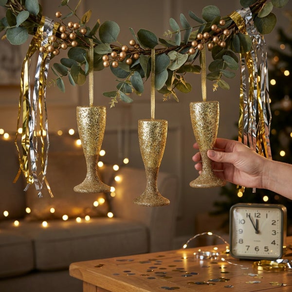 Drei hängende Sektkelch Christbaumkugeln mit Glitzeroptik, dekoriert an einem Zweig mit Lametta für die Weihnachtsdekoration.