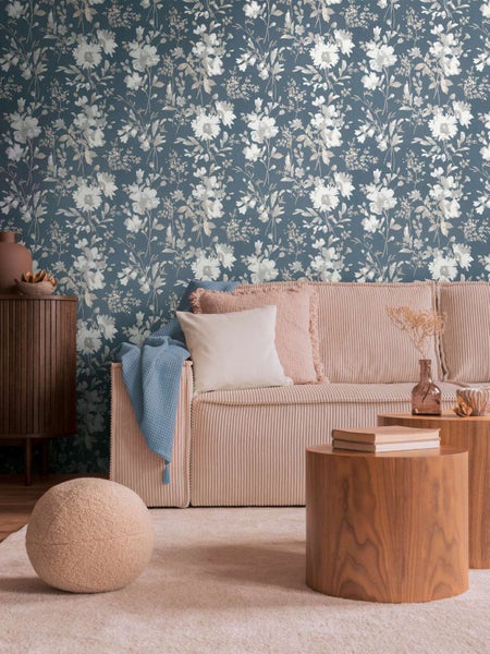 Wohnzimmer mit Vliestapete mit Blumenmuster vor einer Wand, eingerichtet mit einem Sofa, Beistelltischen und dekorativen Wohnaccessoires.