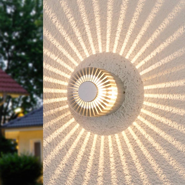 Runde LED-Außenwandleuchte mit strahlenförmigem Lichteffekt an einer strukturierten Hausfassade.