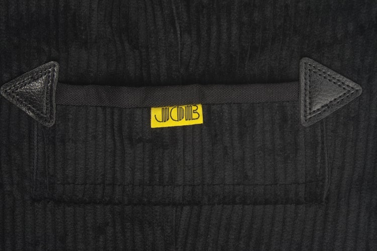 Detailansicht einer schwarzen Cordhose mit Tasche und JCB Logo