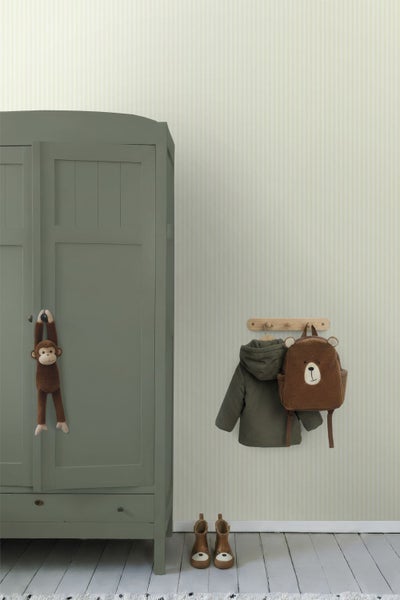 Kinderzimmer mit vertikal gestreifter Tapete, grünem Holzschrank und Wandhaken mit Kinderjacke und Bären-Rucksack.