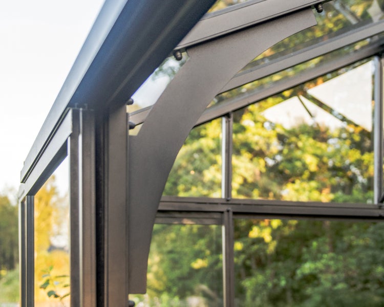 Nahaufnahme einer Metallrahmenkonstruktion eines Gewächshauses mit gebogener Eckverstärkung und Glaselementen.