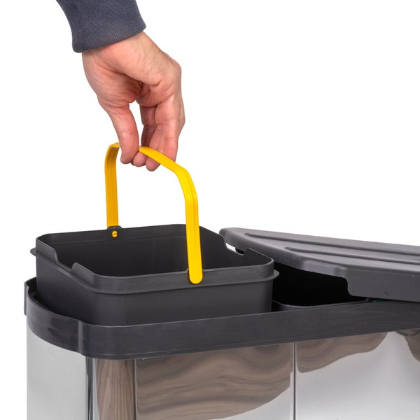 Eine Hand hebt einen schwarzen Inneneimer mit gelbem Henkel aus einem Mülltrennsystem aus Edelstahl.