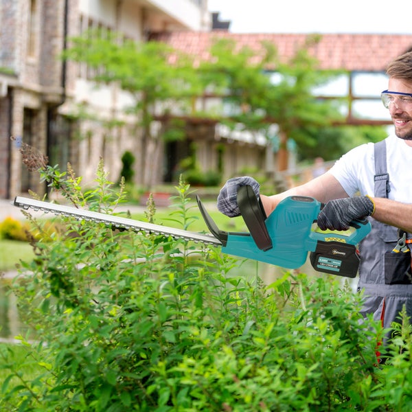 Ein Mann schneidet mit einer Akku-Heckenschere eine Hecke im Garten.