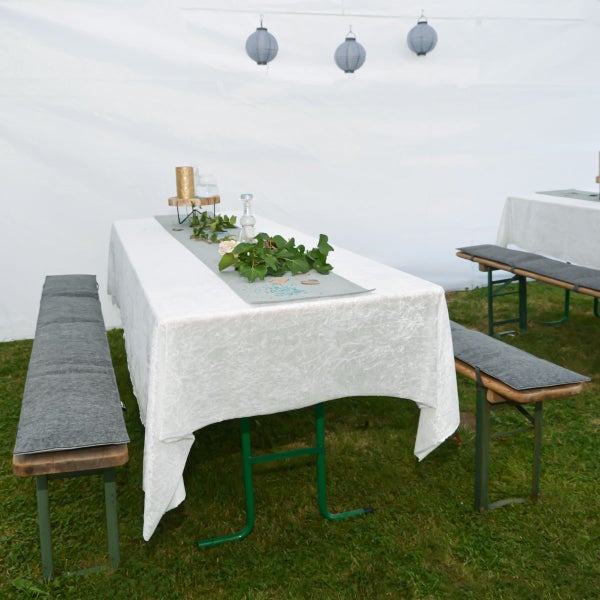 Festzelt mit Bierzeltgarnituren, gedeckt mit Tischdecken, Sitzkissen und Tischdekoration aus Efeu, Kerzen und Lampions an der Decke.