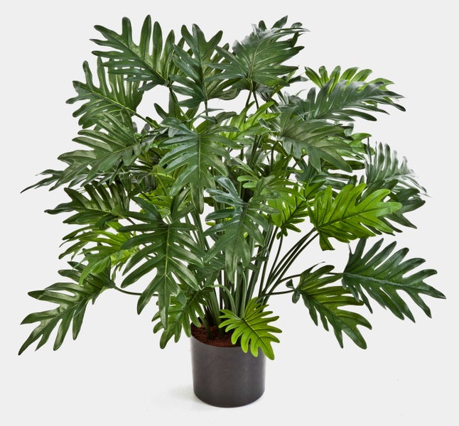Künstlicher Philodendron mit gezackten grünen Blättern in einem schwarzen Topf.