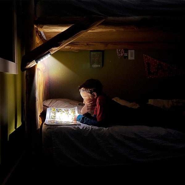 Ein Kind liegt in einem dunklen Holzbett und liest ein Buch mit Hilfe einer angebrachten Lampe.