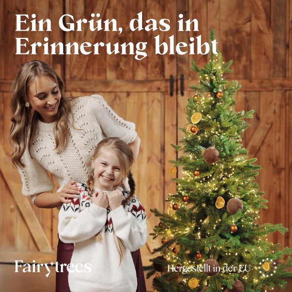 Eine Frau und ein Kind vor einem geschmückten FairyTrees Weihnachtsbaum in einer wohnlichen Umgebung mit Holzvertäfelung und Lichterkette.