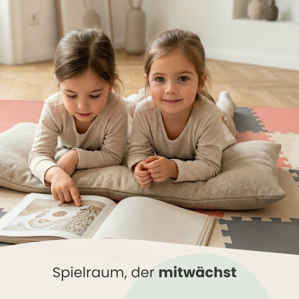 Zwei Kinder liegen auf einem Kissen auf einer Puzzlematte aus Schaumstoff in einem hellen Zimmer und lesen ein Buch.