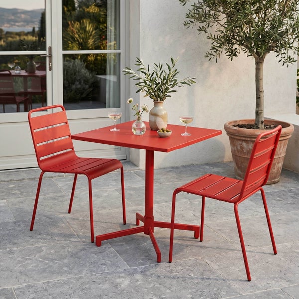 Gartenmöbel-Set bestehend aus einem quadratischen roten Tisch und zwei roten Metallstühlen auf einer hellen Steinterrasse.