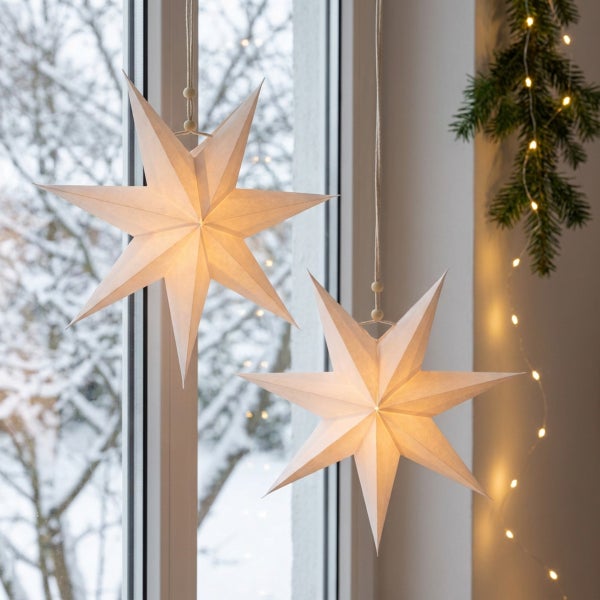 Zwei beleuchtete Papiersterne als weihnachtliche Fensterdekoration hängend vor einem winterlichen Fenster mit Tannengrün.