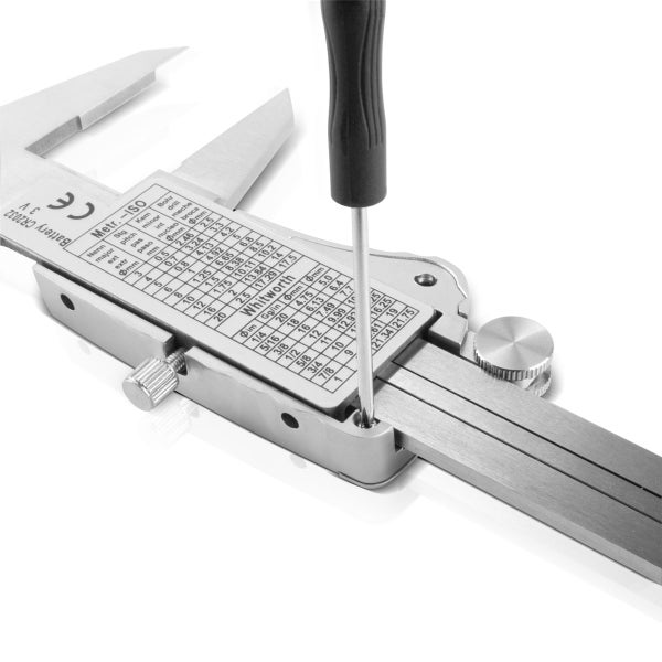 Kleiner Schraubendreher löst eine Schraube an einem digitalen Messschieber aus Metall mit rückseitiger Umrechnungstabelle.