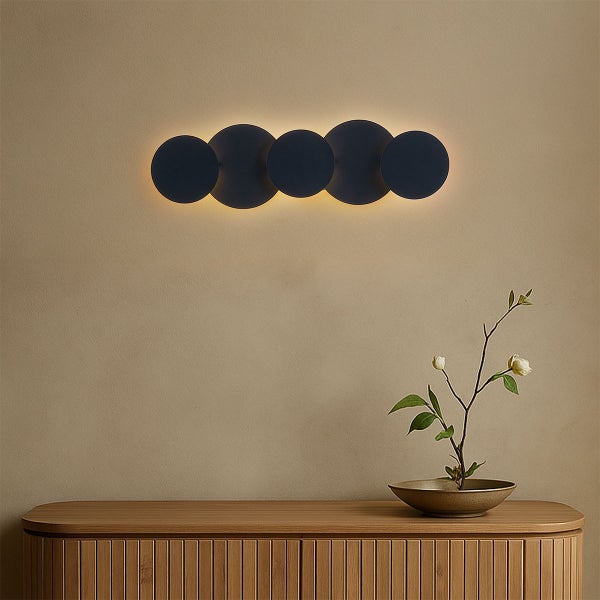 Wandleuchte mit kreisförmigen Elementen über einem Holzschrank mit Blumendekoration