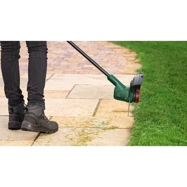 Eine Person verwendet einen Bosch Rasenkantenschneider, um die Rasenkante an einem gepflasterten Gartenweg präzise zu schneiden.