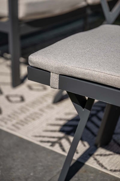Nahaufnahme eines Gartenstuhls mit grauem Metallgestell und gepolstertem Sitzkissen aus grauem, strukturiertem Stoff.