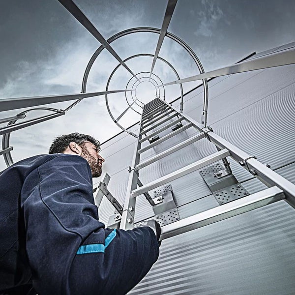 Mann steigt eine fest installierte Leiter mit Rückenschutz an einer Fassade hoch