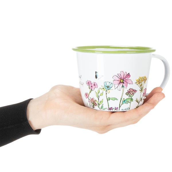 Hand hält eine weiße Tasse mit bunten Blumen und grünem Rand.