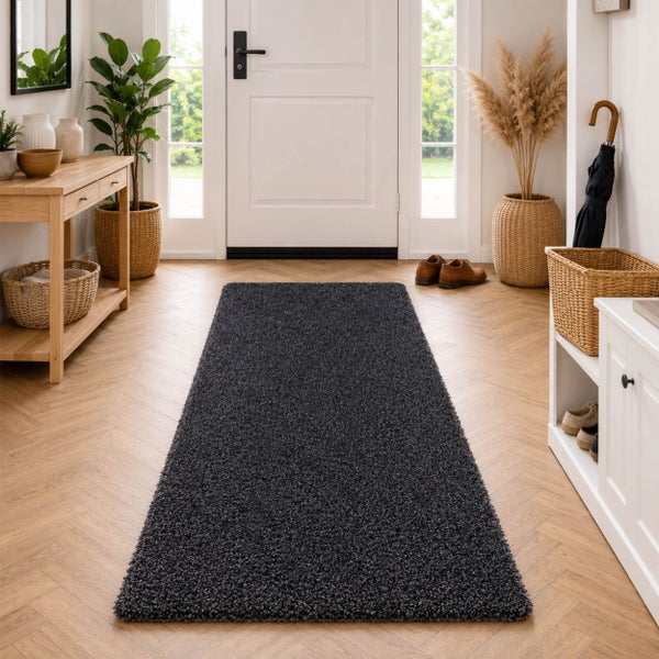 Ein rechteckiger, dunkler Hochflor-Läufer in einem hellen, modern eingerichteten Flur mit einem Holzboden in Fischgrätoptik vor einer Hauseingangstür.