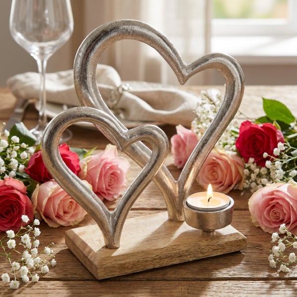 Dekorativer Kerzenhalter mit zwei Herzformen aus Metall auf einem Holzsockel, dekoriert mit Rosen auf einem Tisch.