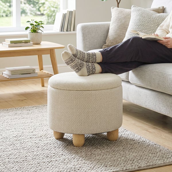 Runder Polsterhocker mit Stoffbezug und Holzfüßen in einem gemütlichen Wohnzimmer.