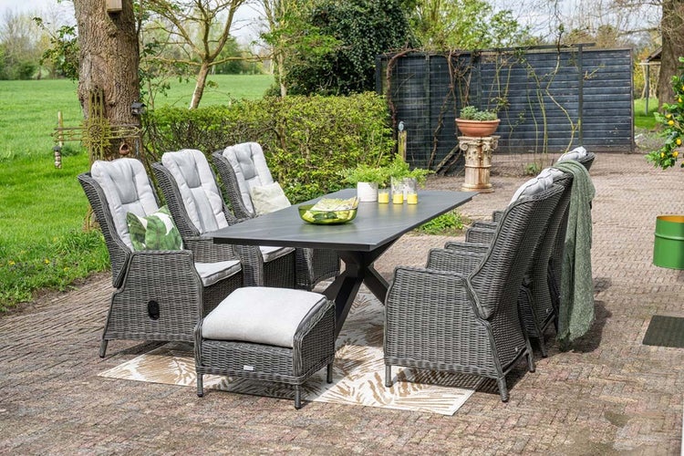 Gartenmöbel-Set bestehend aus einem großen Esstisch mit dunkler Platte, Polyrattan-Sesseln mit hellen Polstern und einem Hocker auf einer Terrasse.