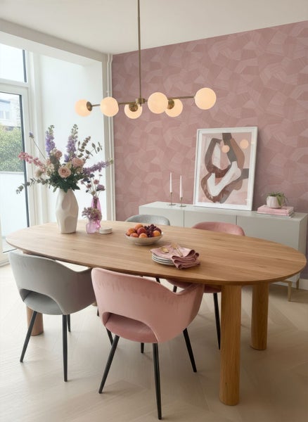 Vliestapete mit geometrischem Muster in Rosa in einem hellen, modernen Esszimmer mit ovalem Holztisch und Samtstühlen.