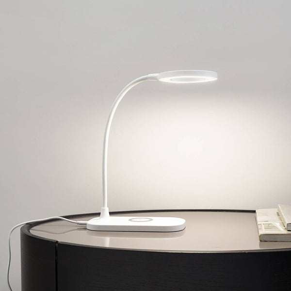 Weiße LED-Schreibtischlampe mit flexiblem Hals, ringförmigem Leuchtkopf und kabelloser Ladefunktion auf einem Beistelltisch.