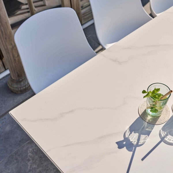 Moderner Gartentisch in Marmoroptik mit weißen Stühlen auf einer hellen, organisierten Terrasse.