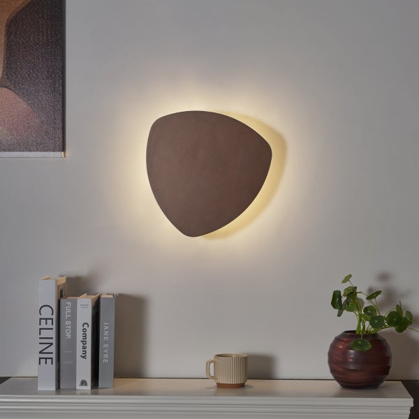 Braune Wandleuchte in dreieckiger Form neben Dekorationsgegenständen an der Wand montiert