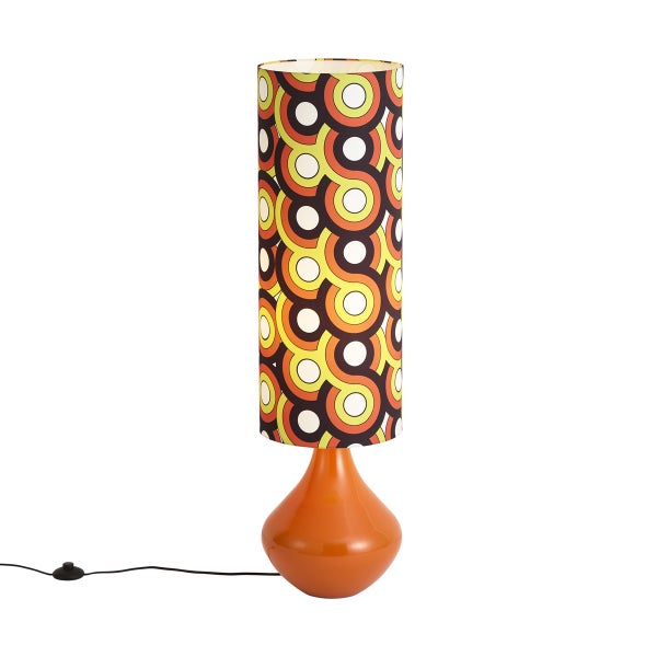 Retro-Tischleuchte mit glänzendem, orangefarbenem Standfuß und hohem, zylindrischem Lampenschirm mit buntem, geometrischem Kreismuster.