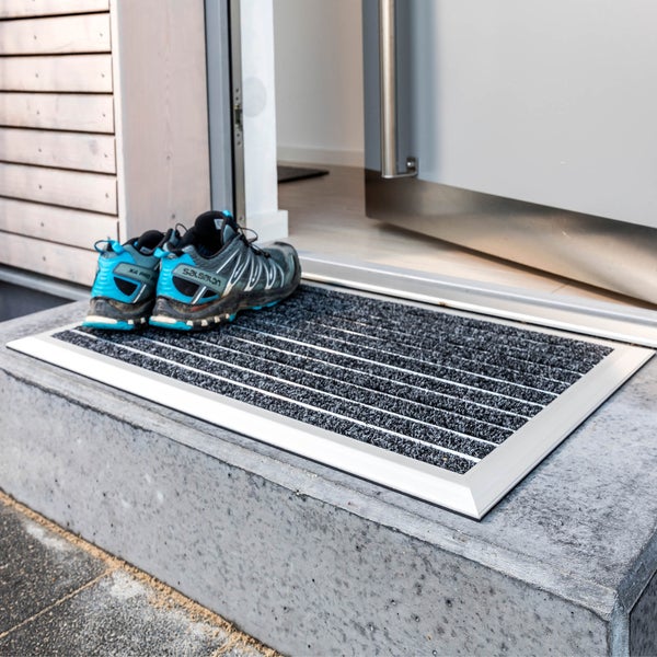 Eingangsmatte mit Aluminiumrahmen und Rips-Einlage vor einer Haustür auf einer Betonstufe.