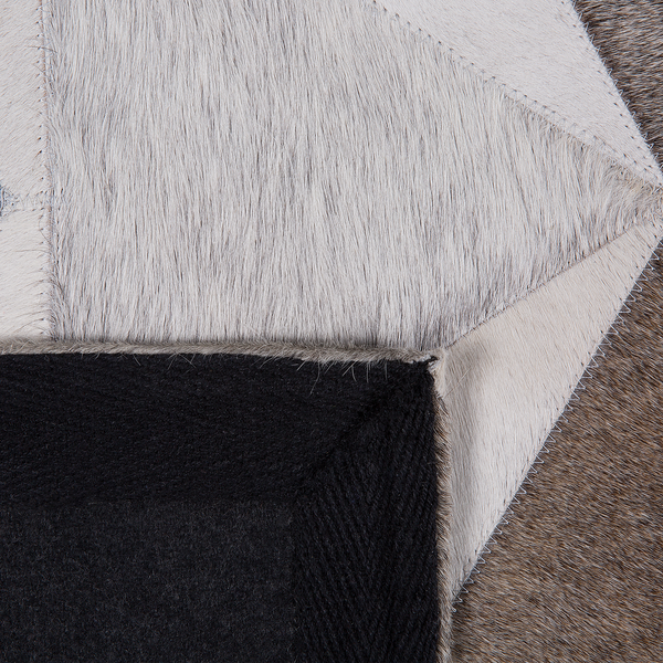Detailaufnahme eines Patchwork-Teppichs aus Kuhfell mit geometrischen Mustern, Zickzack-Nähten und einer schwarzen Filz-Rückseite.