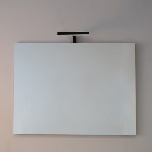 Rechteckiger Spiegel mit einer darüber montierten schwarzen LED-Aufsatzleuchte an einer Wand.