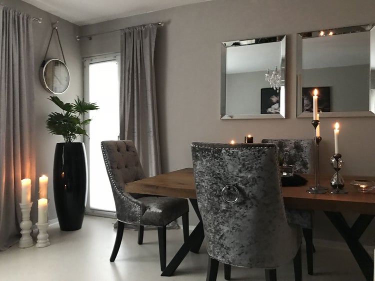 Modernes Esszimmer mit massivem Holztisch, gepolsterten Samtstühlen, Wandspiegeln und dekorativer Kerzenbeleuchtung.