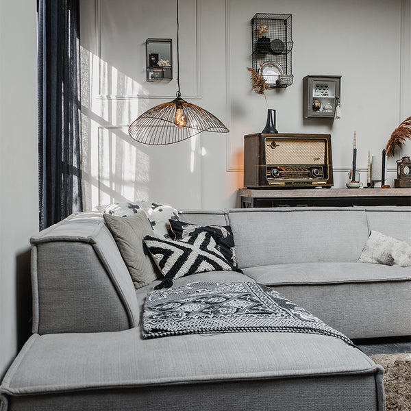 Wohnzimmer mit grauem Ecksofa, Zierkissen, Decke, Lampe und einem alten Radio.