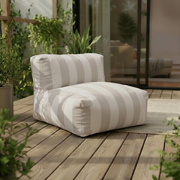 Gestreifter Outdoor-Sitzsack auf einer Holzterrasse umgeben von grünen Pflanzen vor einer Glasfront.