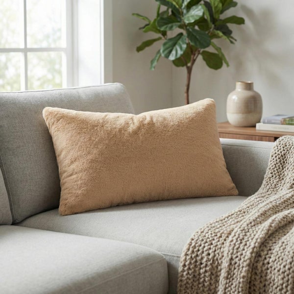 Rechteckiges Dekokissen mit weicher Plüschoberfläche auf einem grauen Sofa in einem hellen Wohnzimmer.