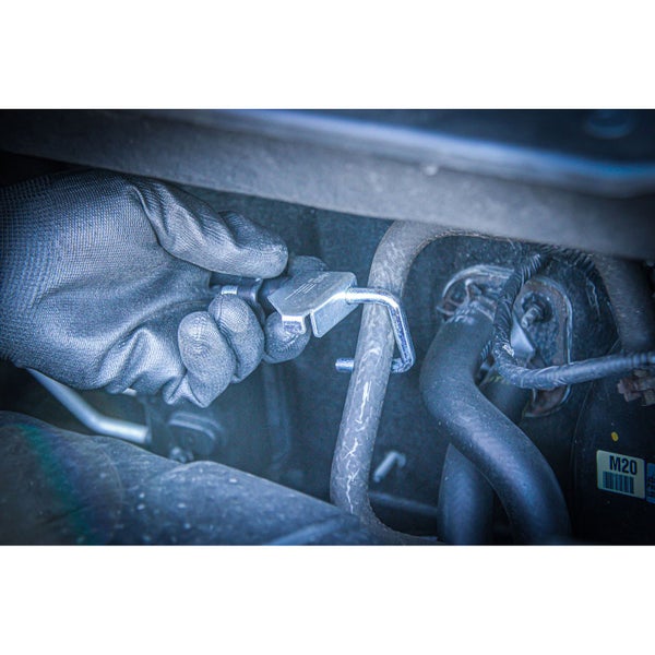 Eine Hand mit einem Handschuh befestigt eine Schlauchklemme an einem Schlauch in einem Motorraum.